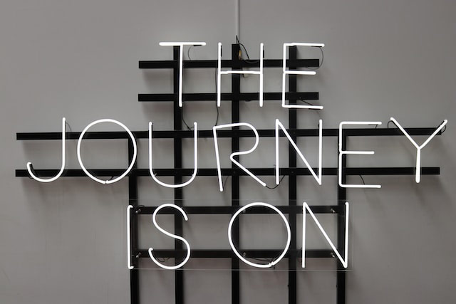 a white neon sign on a gray wall that says 'The Journey Is On'