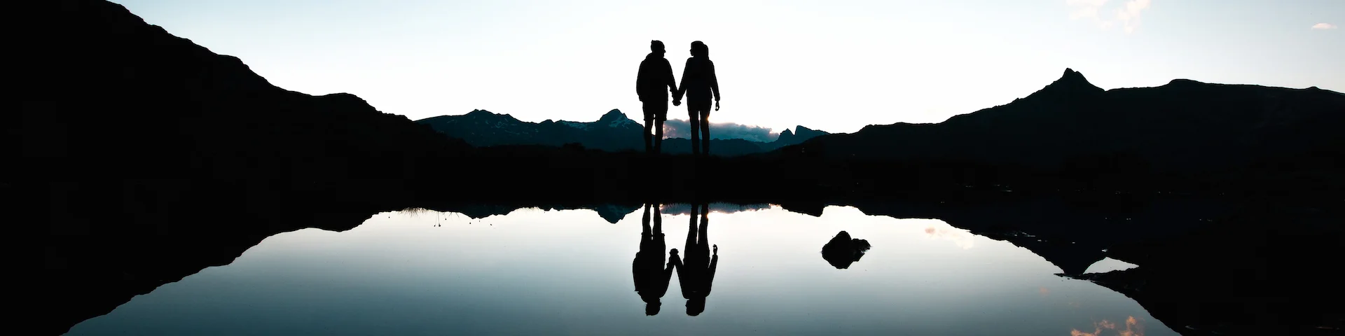silhouette of a couple holding hands next to a lake
