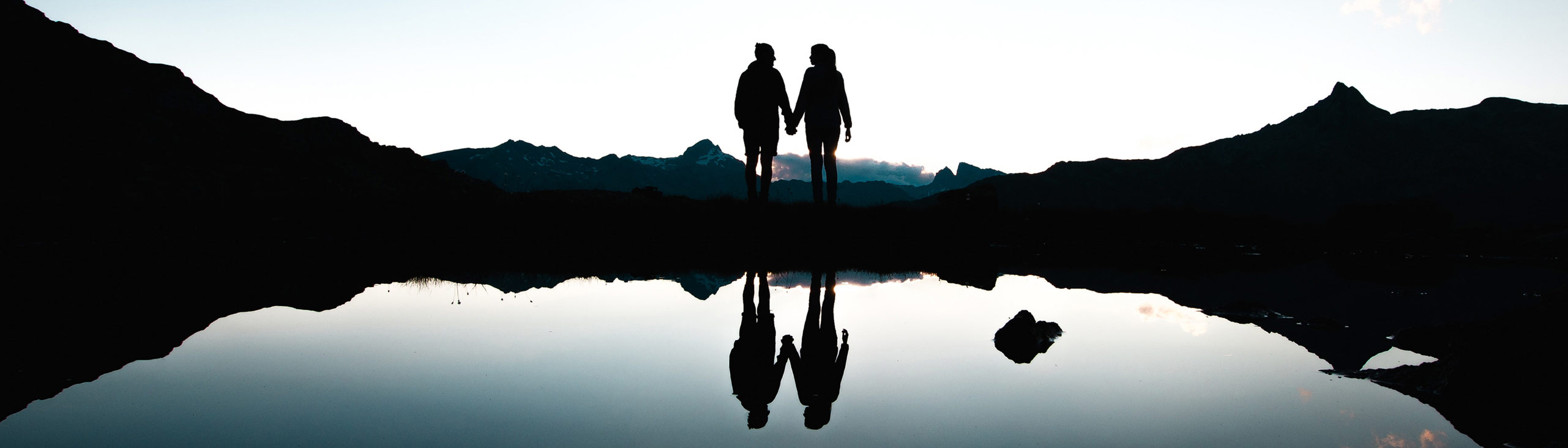 silhouette of a couple holding hands next to a lake