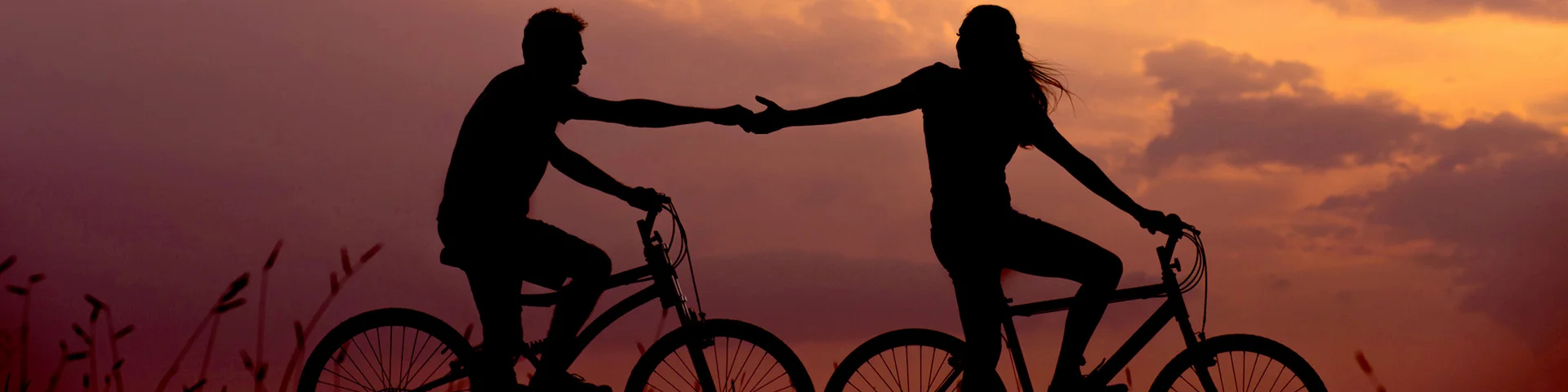 two people on bikes, one is in front of the other, with arms outstretched to hold hands