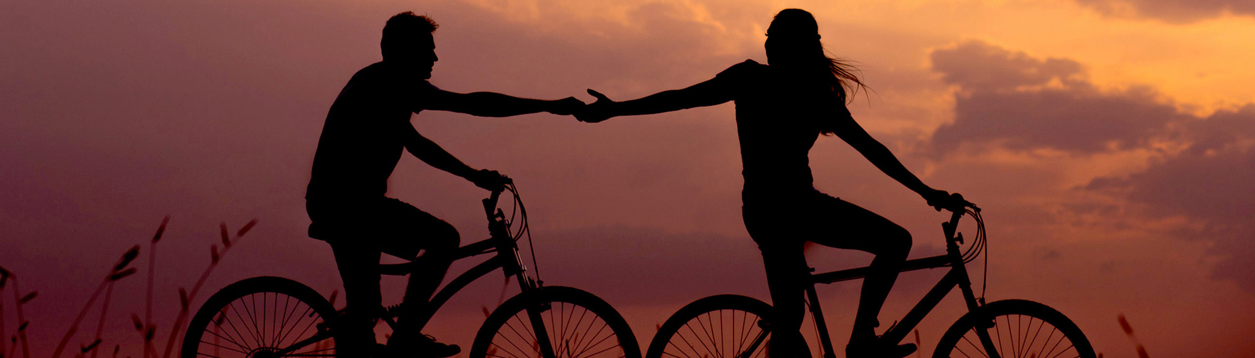 two people on bikes, one is in front of the other, with arms outstretched to hold hands